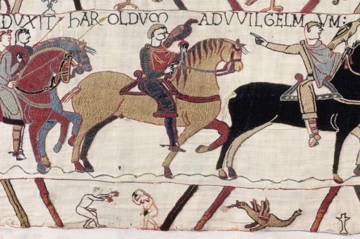 A section of embroidered fabric showing men on horseback. In the corner is an embroidered naked man.