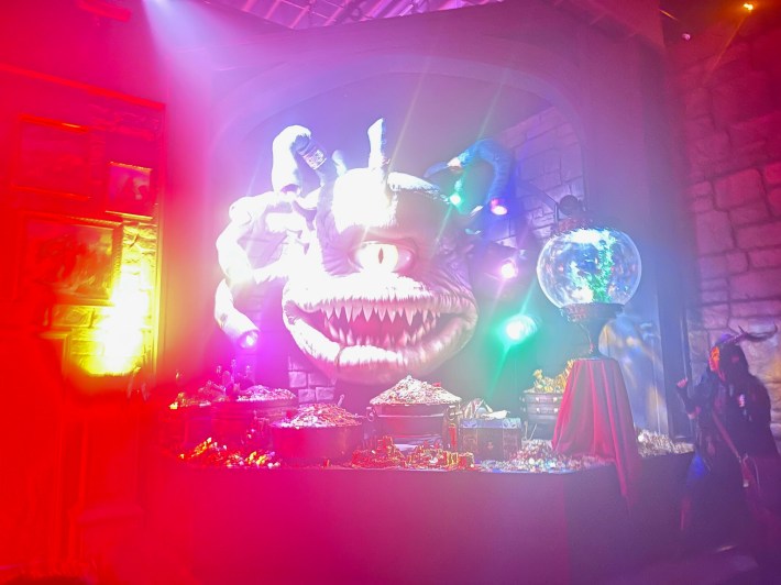 A woman with horns poses next to a huge monster with one large eye over its mouth and many tentacles surrounding.