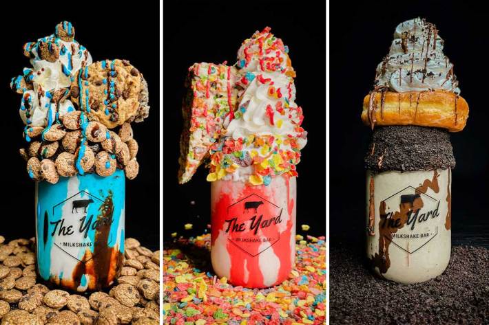 Three ridiculously built milkshakes, with cookies, cake, and donuts stuck in.