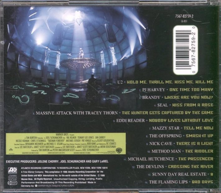 The track listing of a CD, including names like U2, Seal, PJ Harvey, The Flaming Lips, Mazzy Star, the Offspring, Michael Hutchence, Brandy, and Method Man. There is a scene from Batman Forever where a man is surrounded by question marks.