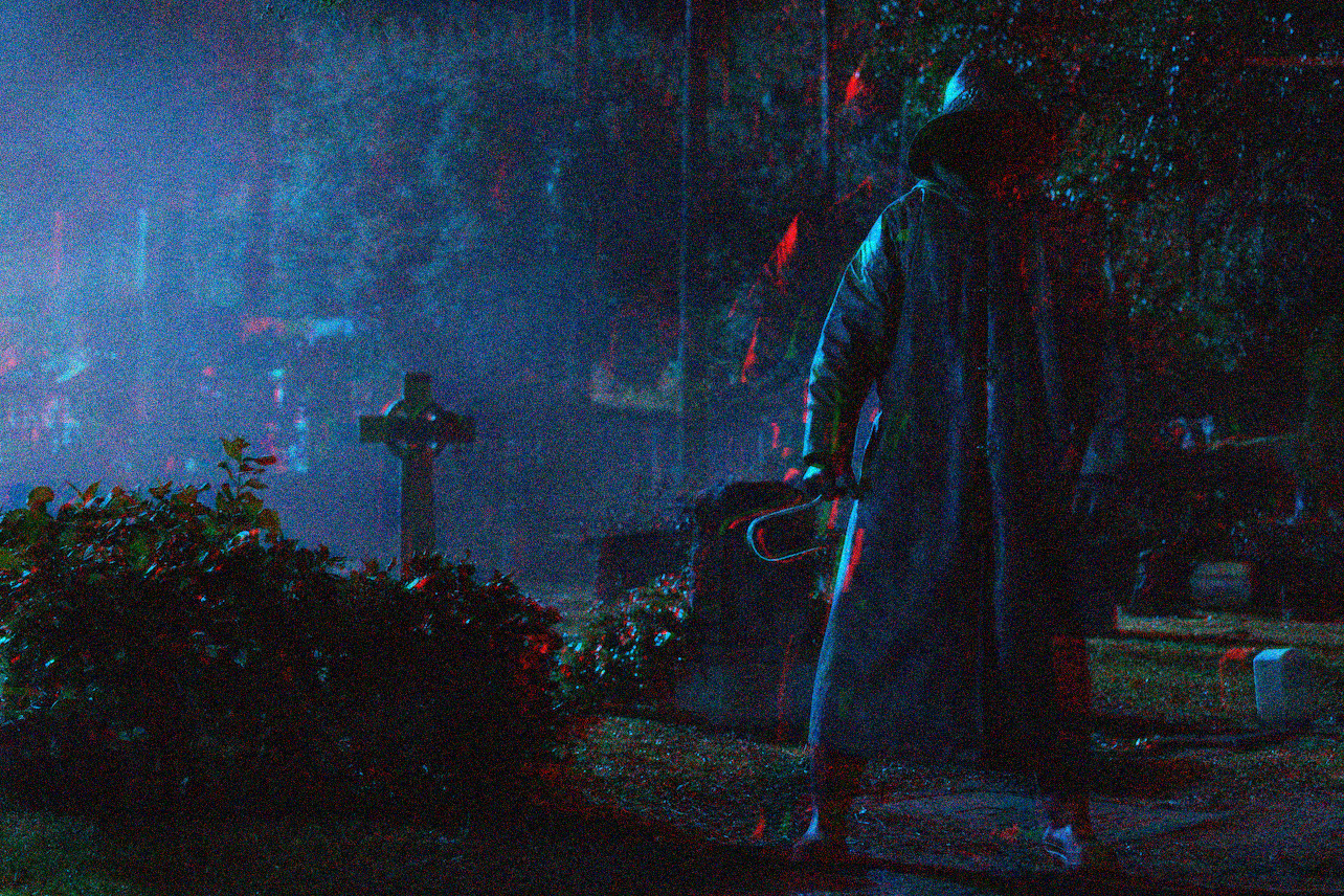 It's night, a man in a fisherman's slicker with a large hook stomps through a cemetery.
