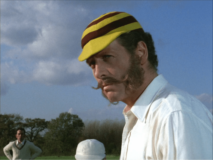 A man with wild mustache and sideburns with a red and yellow striped cap.
