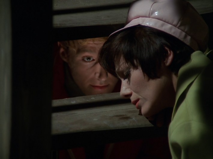 Twenty-Two lies on a set of wooden stairs; Eight is speaking to her from behind the steps