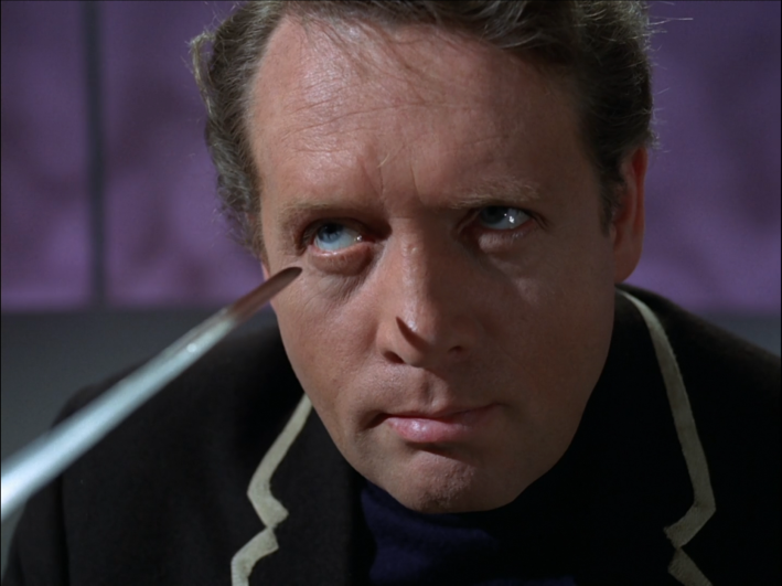A sword is pointed at Six's eye at close range.