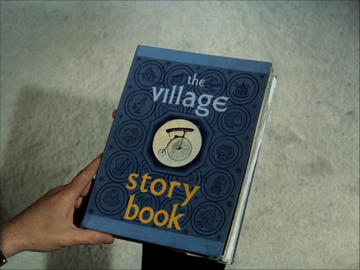 A man's hand holding a book called "The Village Story Book".