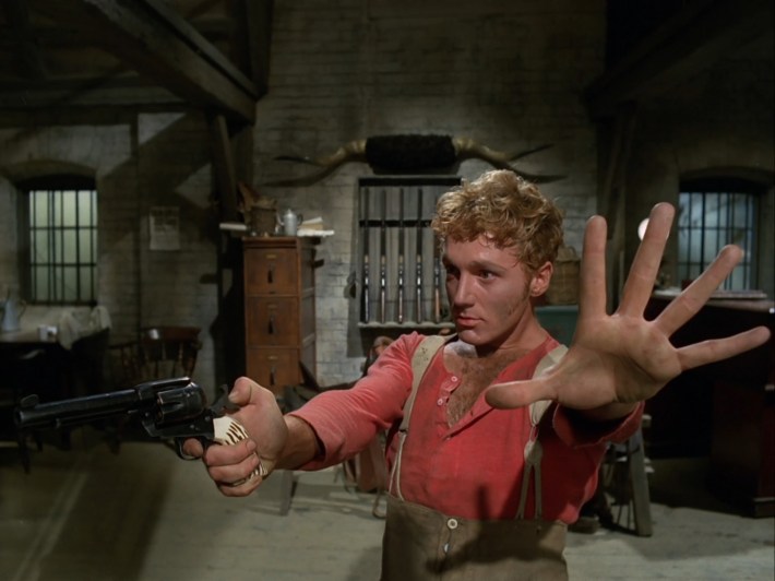 Eight, holding a revolver in one hand and holding his other hand up, palm facing the camera
