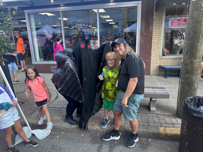 A person in a Mothman costume poses with kids and an older man.
