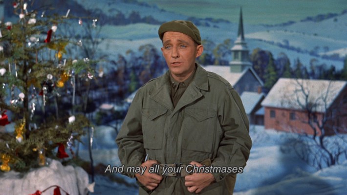 A man in army fatigues in front of a painting of a church. The subtitle reads "And may all your Christmases".