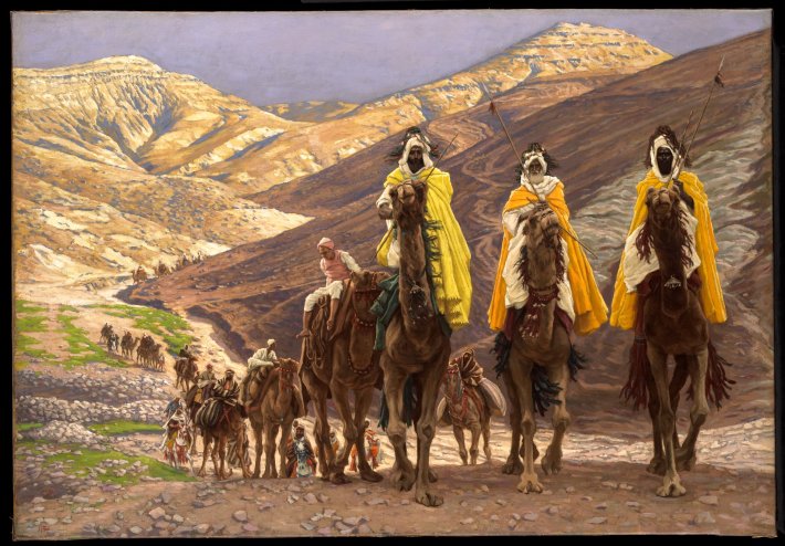 Three men in desert robes ride on camels in the desert, leading a group of riders.