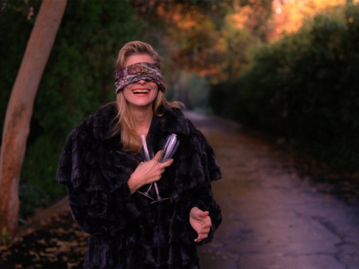 Evelyn with champagne glasses, blindfolded in woods