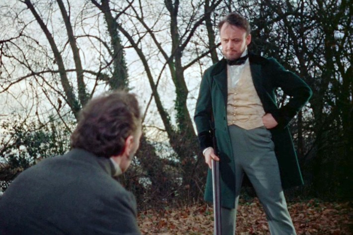 Paul standing with shotgun, wearing trousers